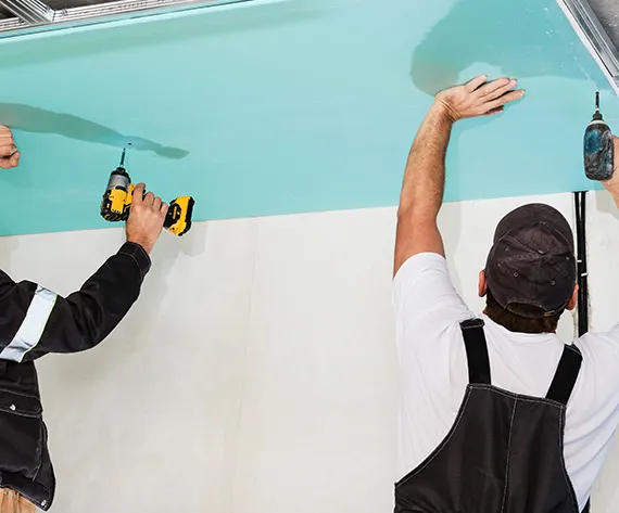 Two men installing drywall in a garage.